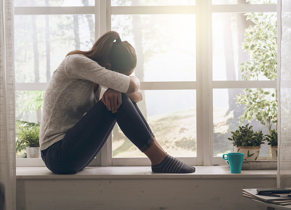 A woman sits on a windowsill with her head resting on her knees. She is feeling lost. She's considering beginning depression counseling in Birmingham, AL 35223 with a depression counselor at Empower Counseling.