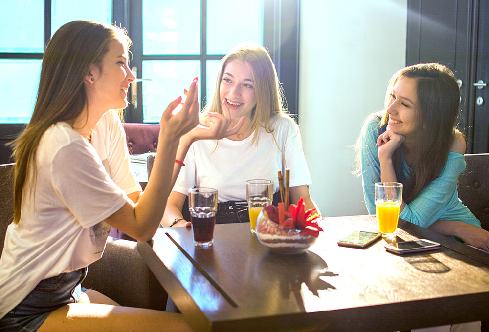 Three girls sit at a table laughing and smiling together at the University of Alabama in Tuscaloosa, AL. They are pleased with their decision to pursue online therapy for college students in Alabama with Empower Counseling for college students in Tuscaloosa, AL.