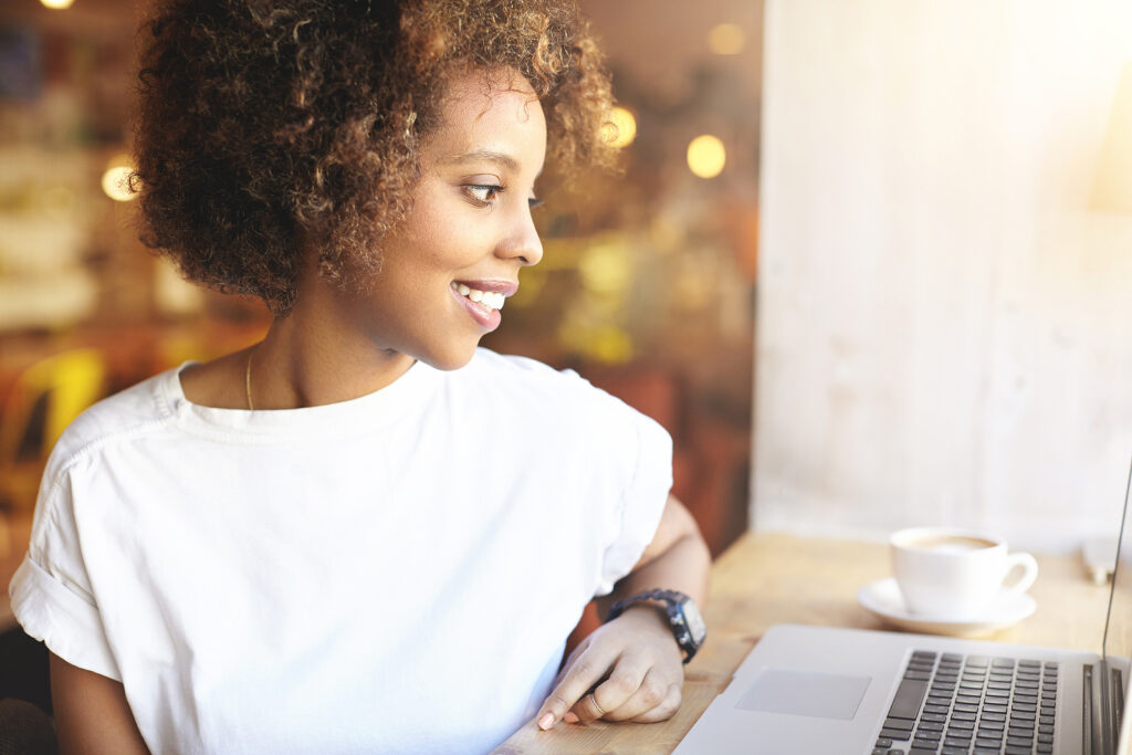A girl smiles while using a laptop. She is happy with her decision to start counseling for college students through online therapy in Auburn, Alabama with Empower Counseling.