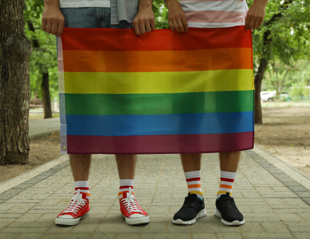 Two young men hold a gay pride flag. Support is key in the healthy development of LGBTQ+ youth. Online counseling for LGBT!+ youth in Alabama can provide support and understanding. 
