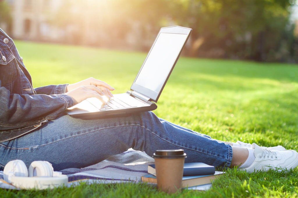 Young woman sitting on a blanket on the grass with her laptop representing someone who is utilizing ACT therapy in Alabama to deal with anxiety and depression. Online therapy in Alabama is easy and effective! 