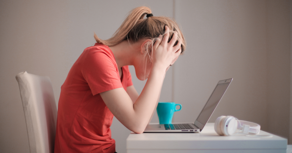Stressed woman looking upset holding her head over her computer. ACT treatment for anxiety near Birmingham, AL can help you reduce stress and overwhelm. Learn more from counselors near Birmingham, Auburn, Tuscaloosa and more.