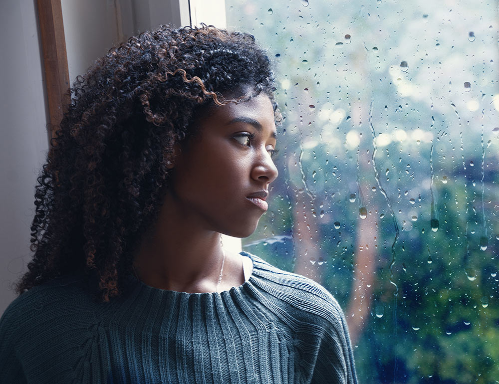 A distressed woman looks out the window while dealing with the effects of Trauma representing someone who could benefit from Trauma Counseling in Birmingham, AL.
