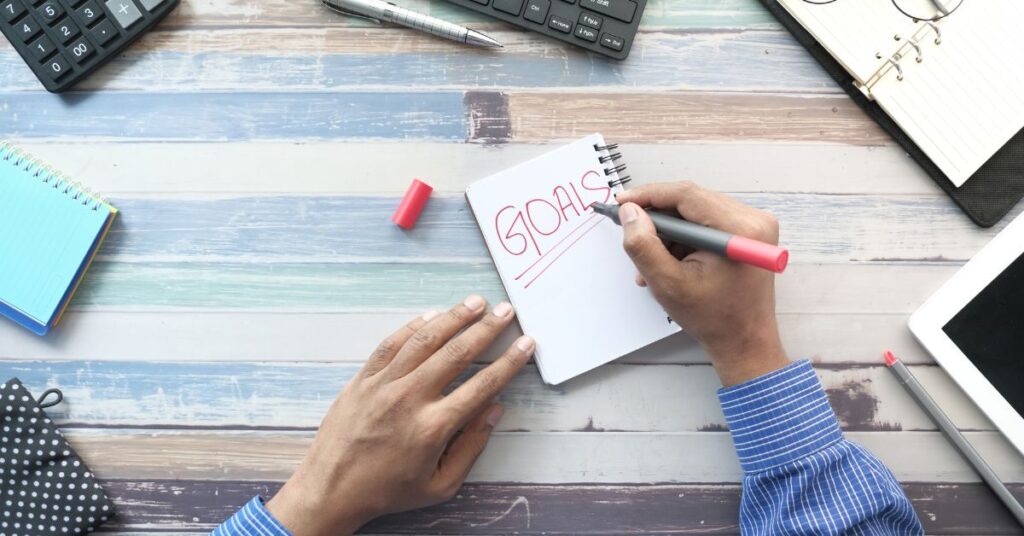 Person writing "goals" on a notepad with a lot of other desk supplies around him. ACT Treatment plans for anxiety can help you feel better from anxiety with the help of an anxiety therapist in Birmingham, AL.