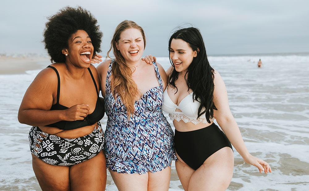 Three laugh together while walking through the ocean. They are feeling better after starting counseling for college students with Empower Counseling through online therapy in Auburn, AL.