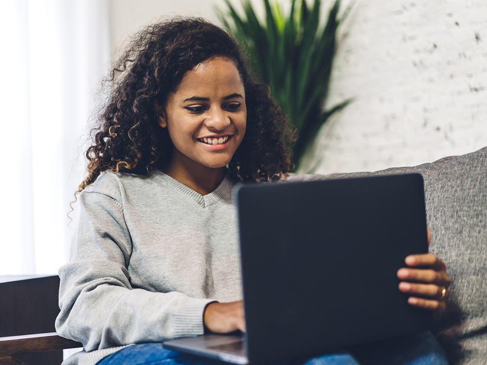 A young woman smiles while looking at her laptop. She is satisfied with her choice to start counseling for life transitions with Empower Counseling in Birmingham, AL 35532