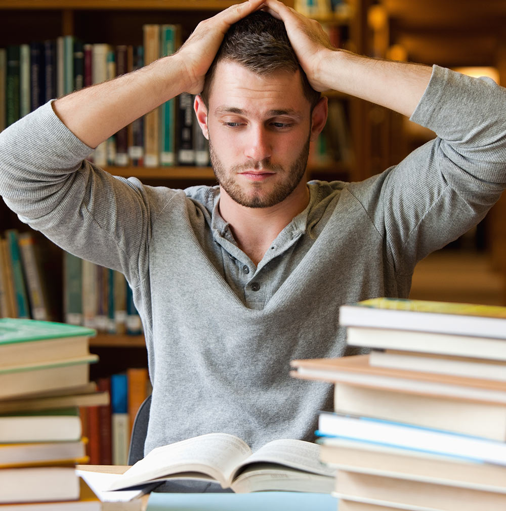 A male college student sits in a library looking overwhelmed. He is considering beginning counseling for college students in Alabama with Empower Counseling.