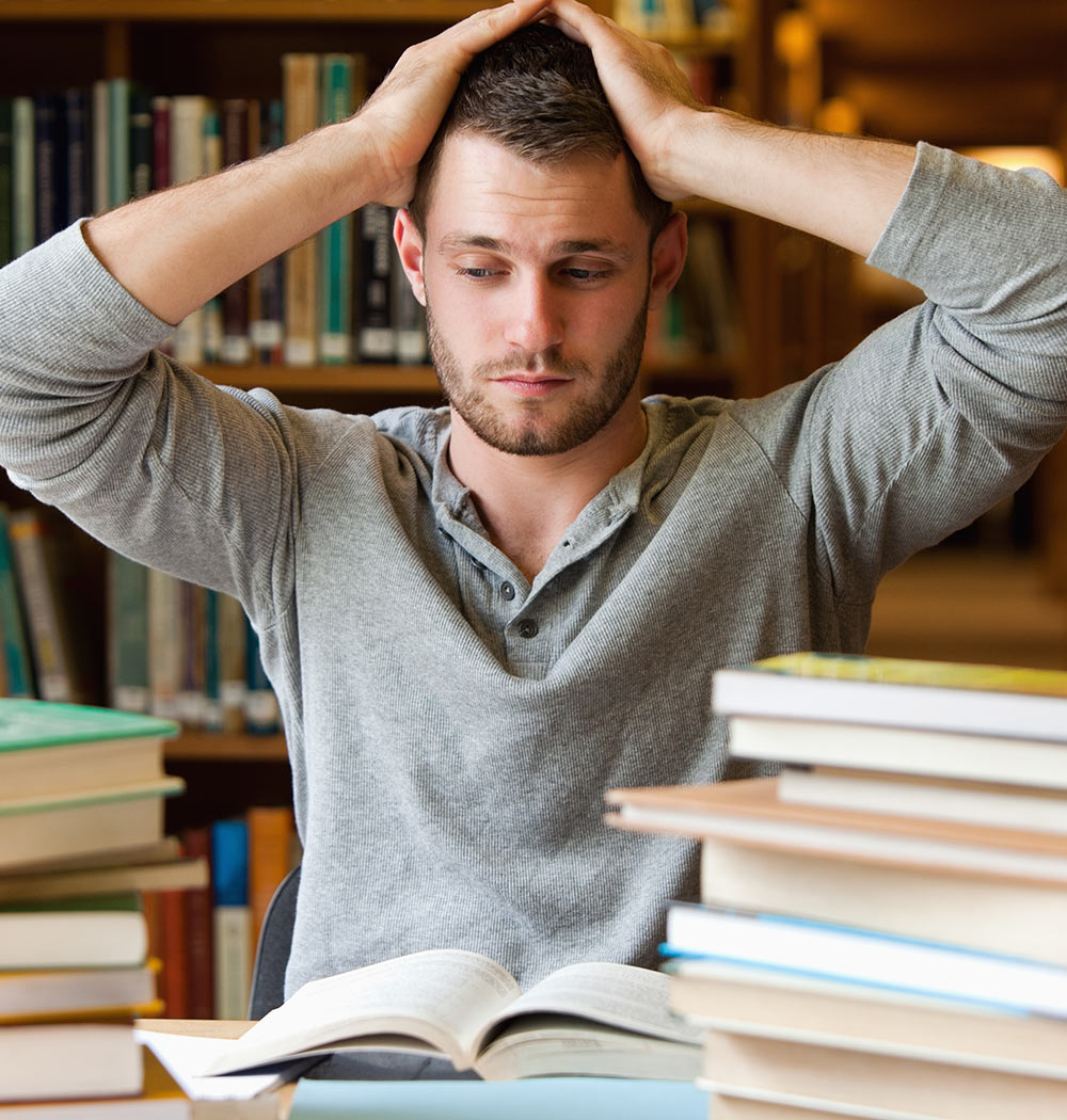 A male college student sits in a library looking overwhelmed. He is considering beginning counseling for college students in Alabama with Empower Counseling.