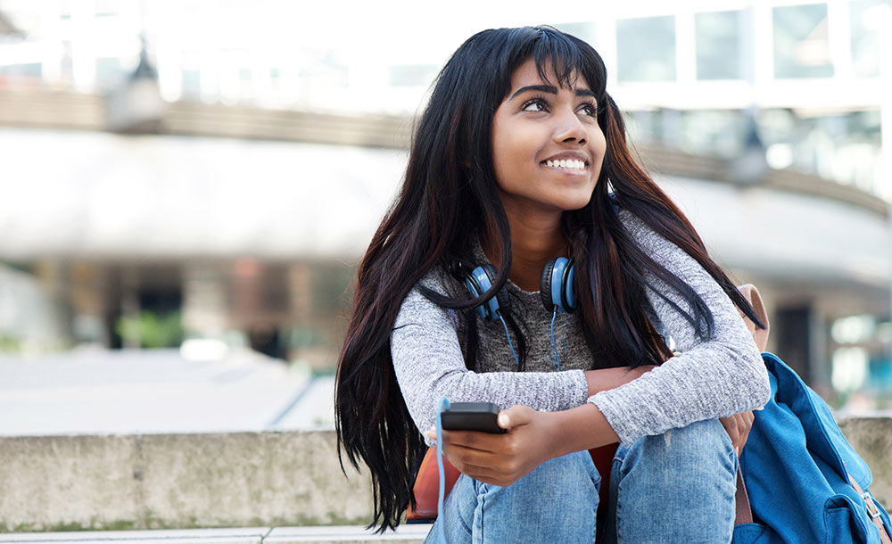 A female college student is sitting on the ground smiling. She is feeling much happier after beginning counseling for college students in Birmingham, AL with Empower Counseling.
