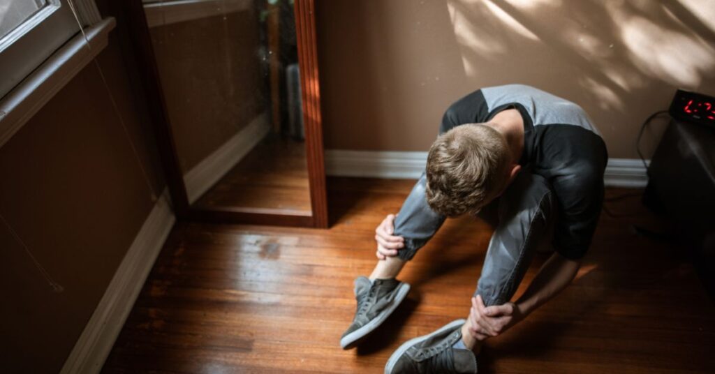An anxious young man sitting on the floor looking down