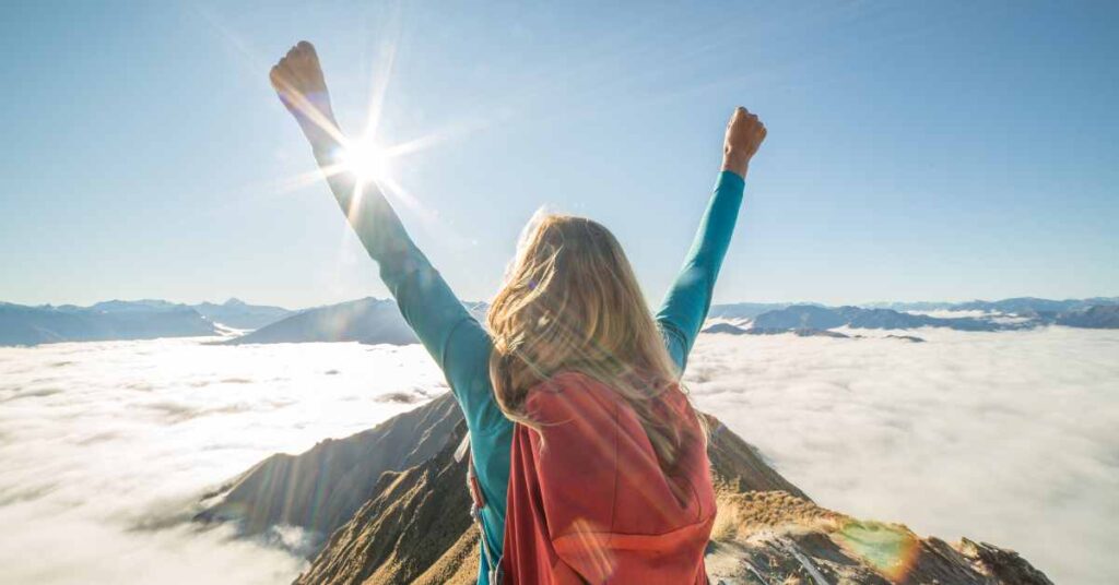 a woman with arms outstretched on summit of mountain