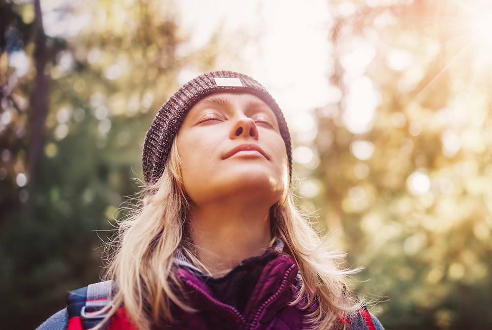 Image of a blonde woman closing her eyes and looking up with a smile while standing in the forest. If you struggle with depression due to trauma, learn how EMDR therapy in Birmingham, AL can help!