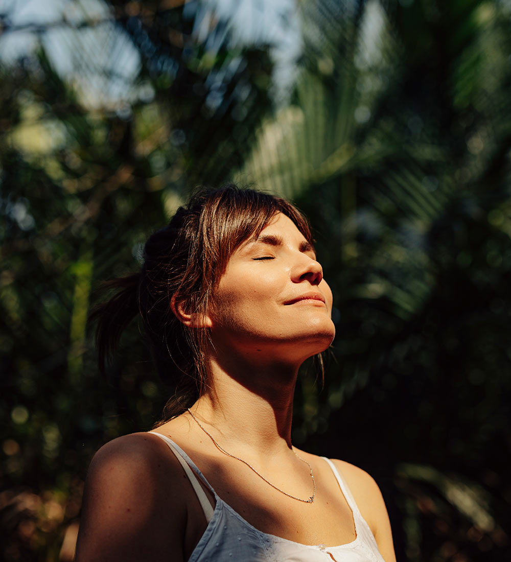 Image of a peaceful woman smiling and closing her eyes standing outside with the sun shining on her face. Discover how you can effectively cope with past trauma with the help of EMDR therapy in Birmingham, AL.
