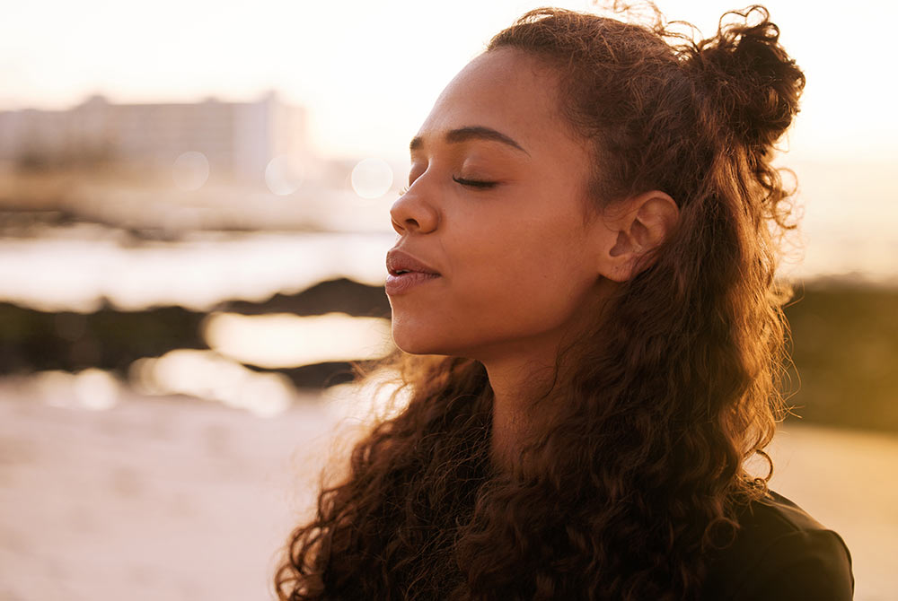Image of a peaceful woman closing her eyes while the sun shines on her face near the ocean. Begin seeing improvements in your trauma symptoms with the help of EMDR therapy in Birmingham, AL.