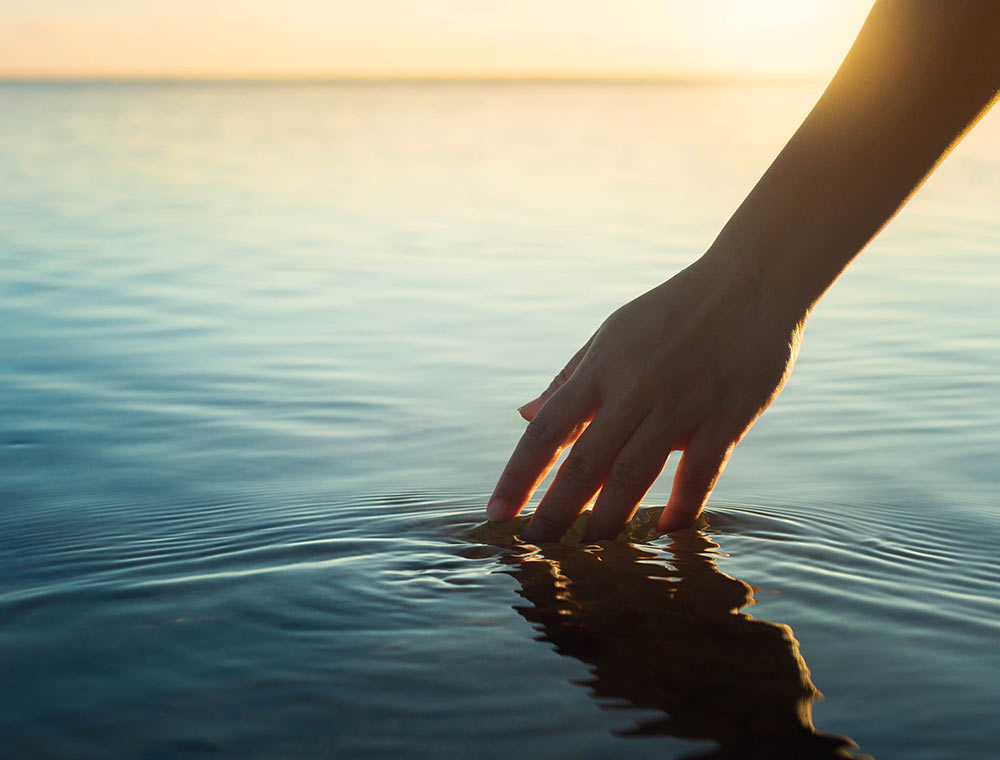 Image of a hand touching water causing ripples while the sun shines. Work with an EMDR therapist to battle the trauma you face with EMDR therapy in Birmingham, AL.