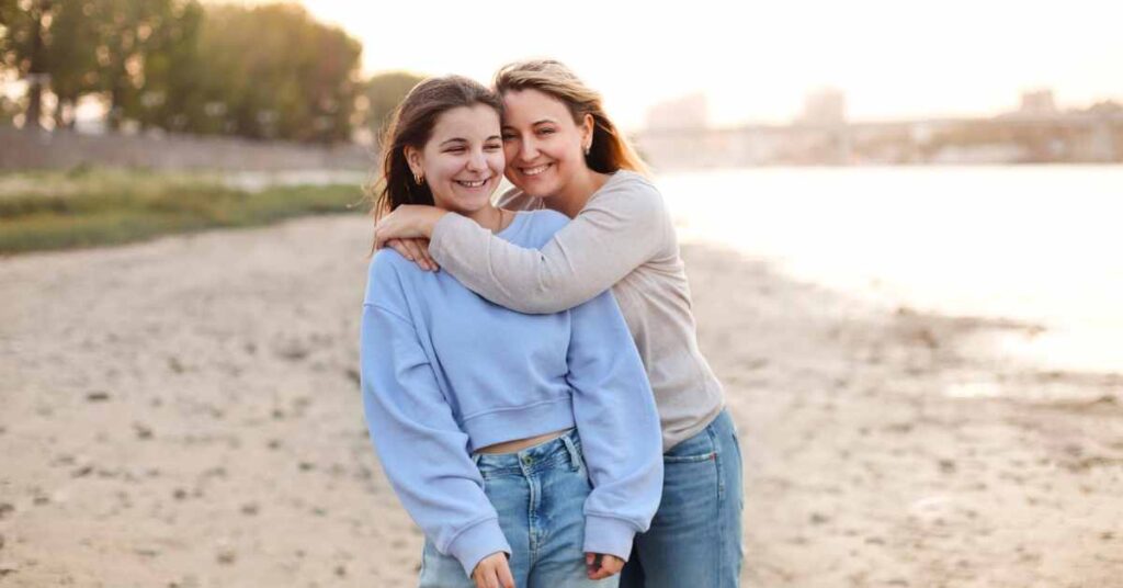 a mom hugging her teen daughter on the beach