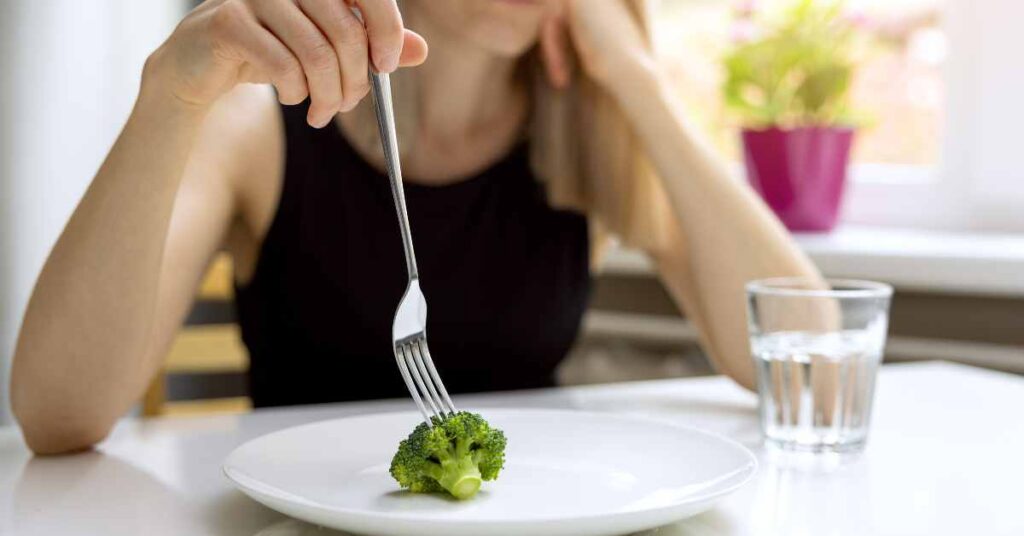 a woman with 1 piece of broccoli on her plate and a glass of water/Eating Disorder Treatment/ Birmingham Al/ Lucia Haladjian