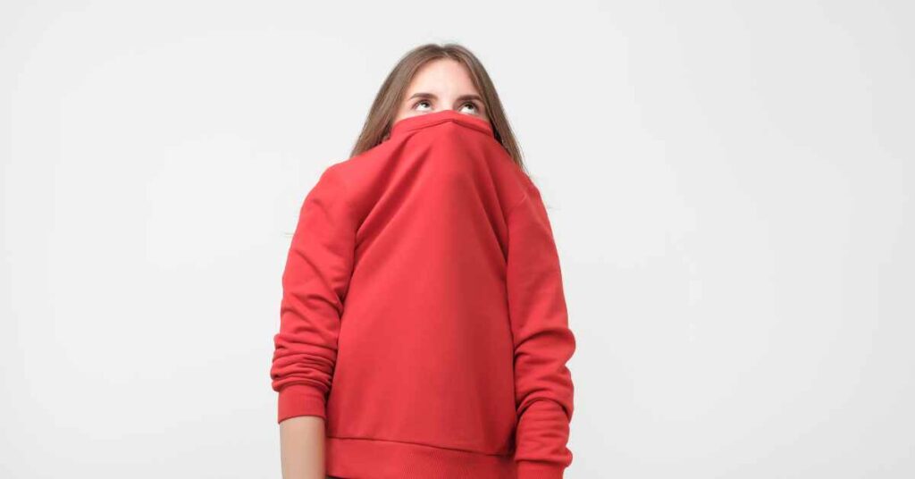 a woman hiding her face in her sweatshirt because of social anxiety/ perfectionism and anxiety counseling/ Birmingham