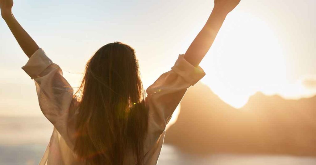 a woman who has overcome her anxiety with raised arms toward the sun
