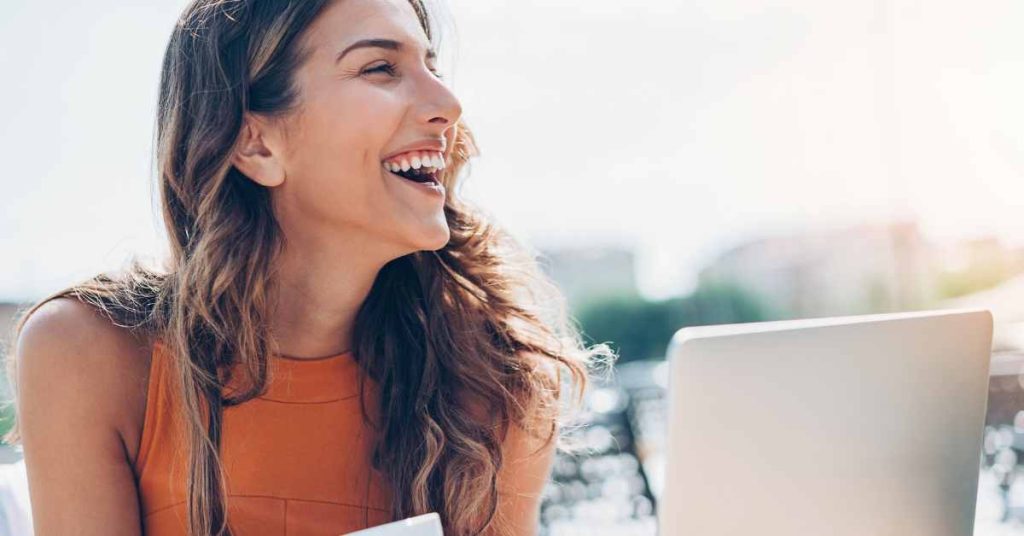 a woman laughing with her laptop in front of her