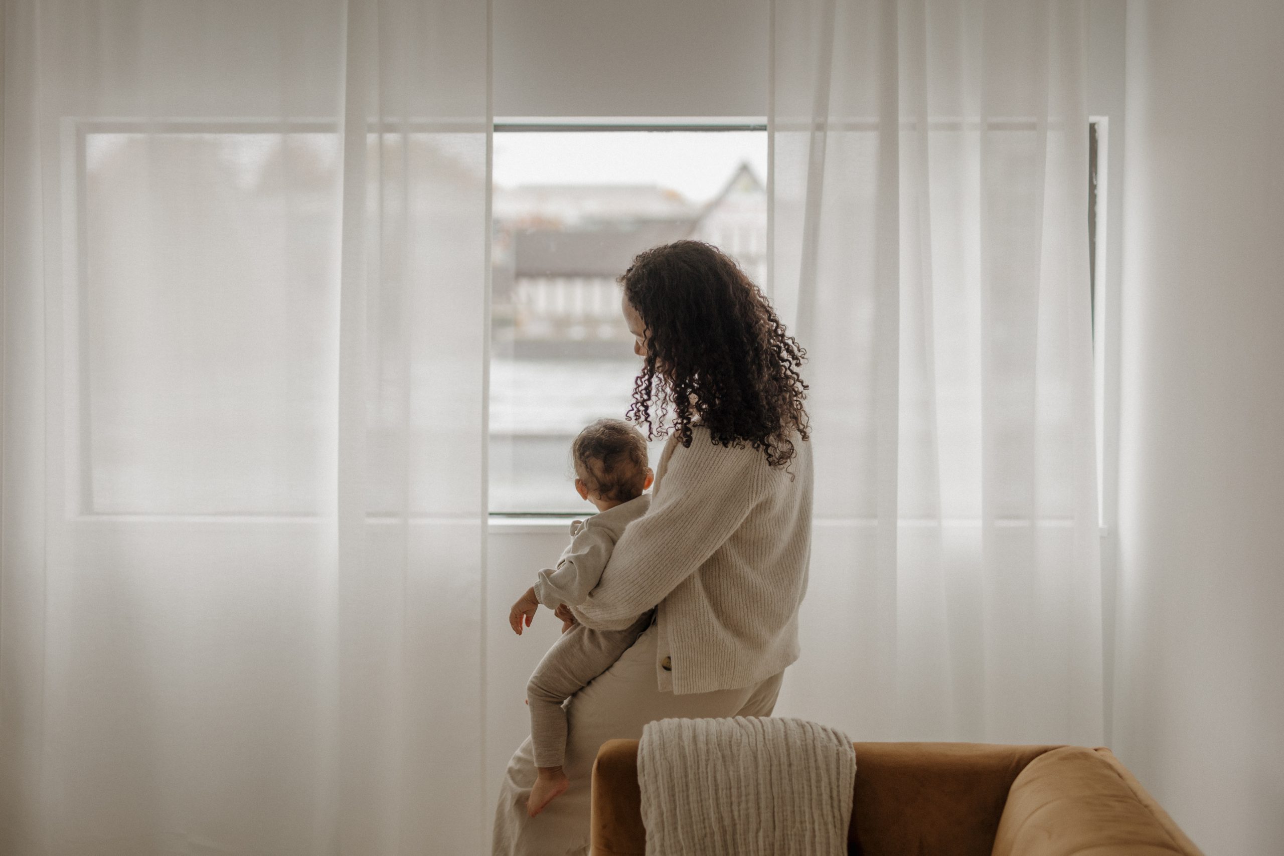 a mom holding her baby looking out the window/ postpartum intrusive thoughts/ Empower Counseling/ Anna Mills Fleenor/ Birmingham/ 35223